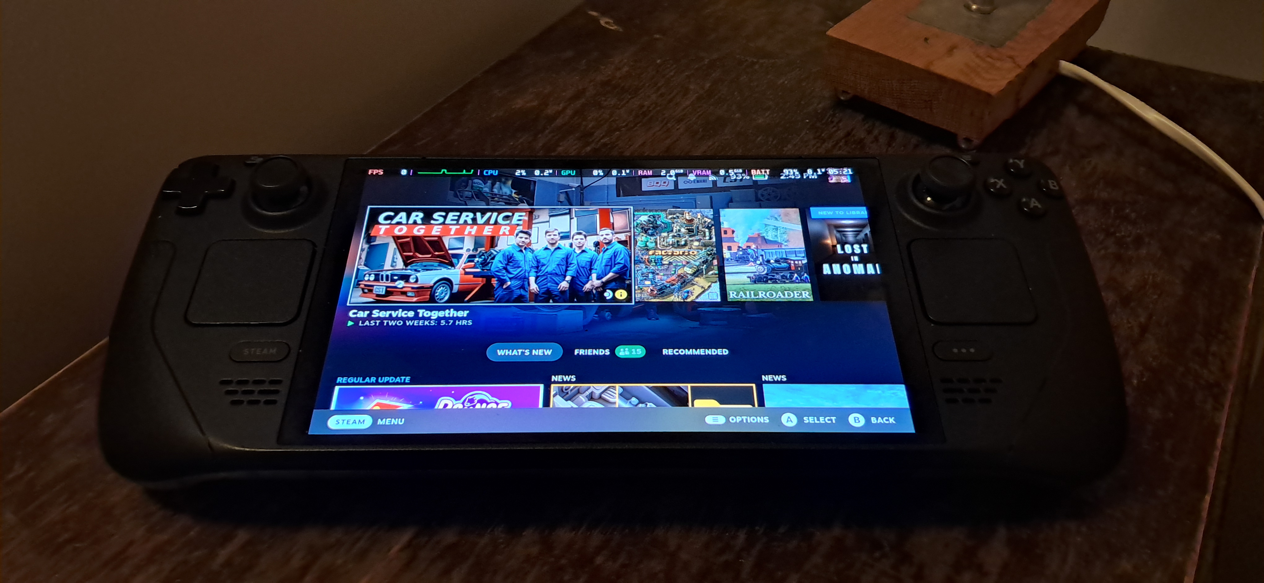 Real photograph of a Steam Deck OLED portable PC running SteamOS, showing its controls and home screen